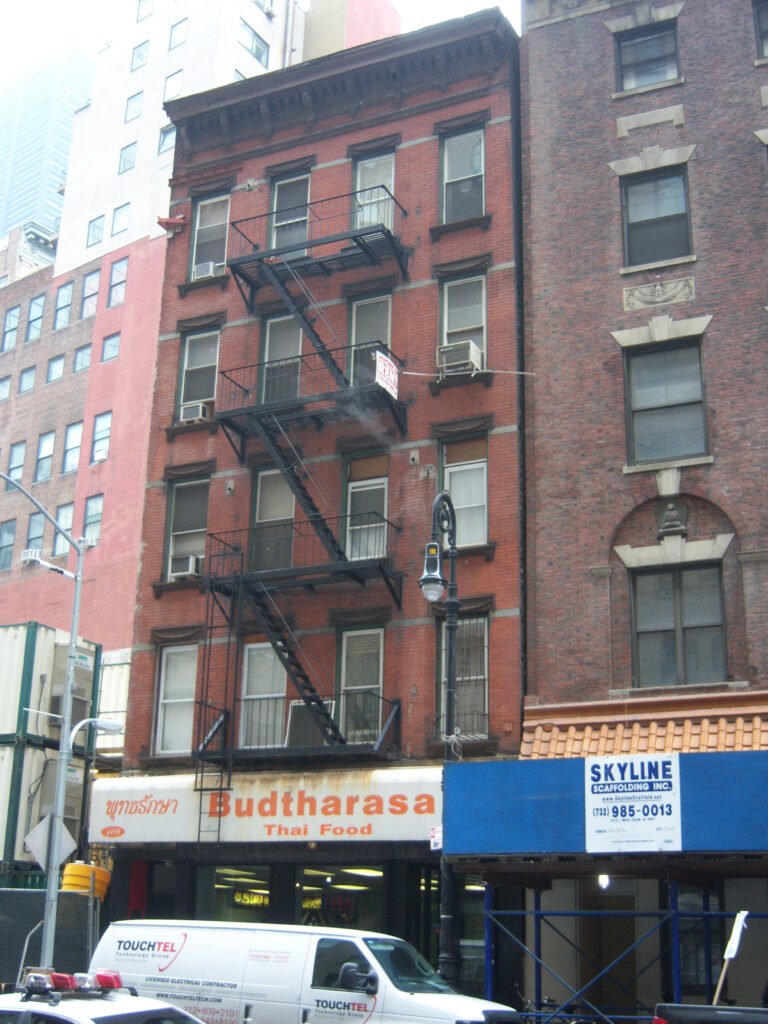 The red-brick 1885 tenement at 109 Washington Street, with fire escapes and a ground-floor restaurant, around 2012