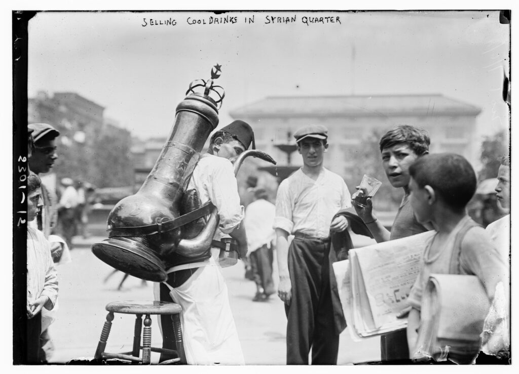 A drinks seller with a large brass urn on his back serves boys in New York's Syrian Quarter, early 1900s