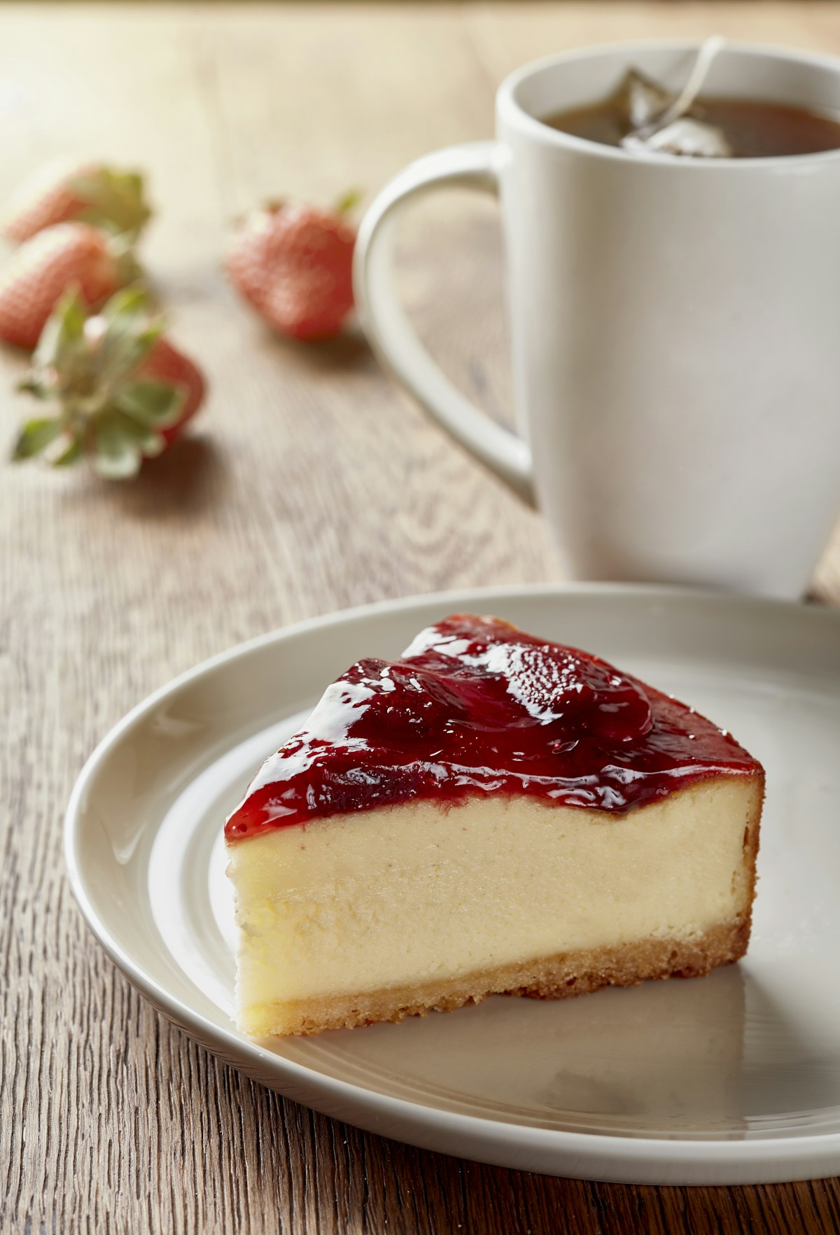 A slice of New York cheesecake on a plate beside a cup of coffee