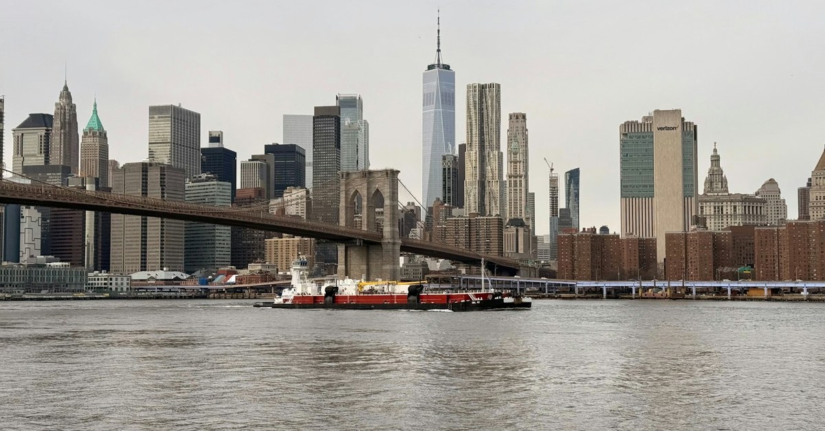 Working barge on New York Harbour with the Brooklyn Bridge and Manhattan skyline behind