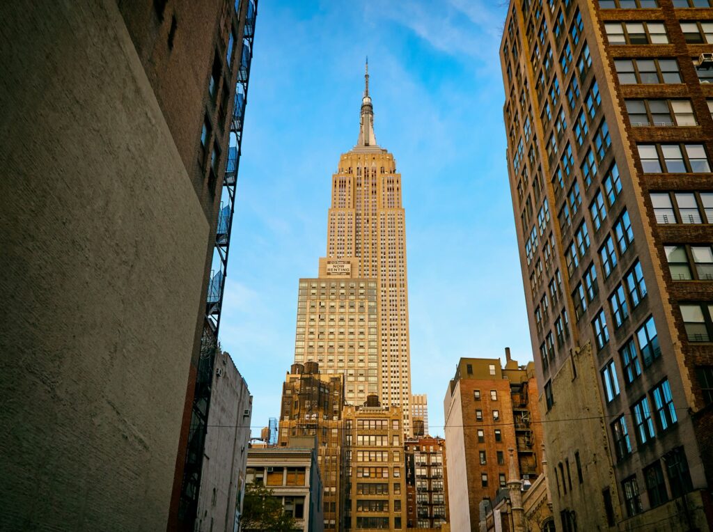 The Empire State Building rising above older Midtown buildings against a blue sky